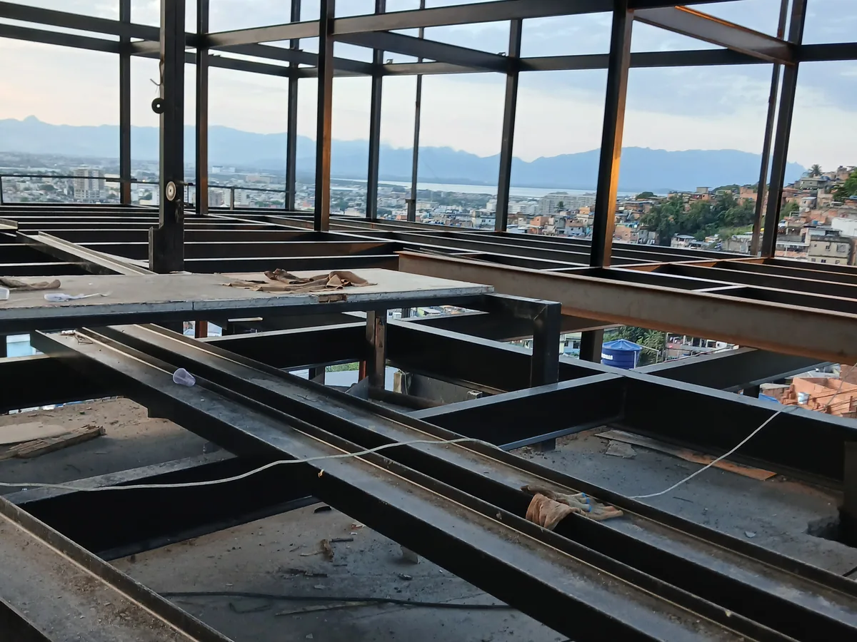 Vigas e pilares metálicos de pavimento em construção, com lajes em steel deck e cidade ao fundo
